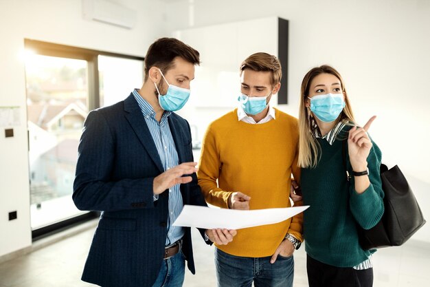 Couple communicating with real estate agent while examining blueprints of a new apartment during COVID19 pandemic