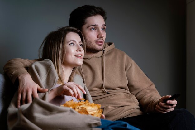 テレビを見たり、チップを食べたりするソファの上のカップル
