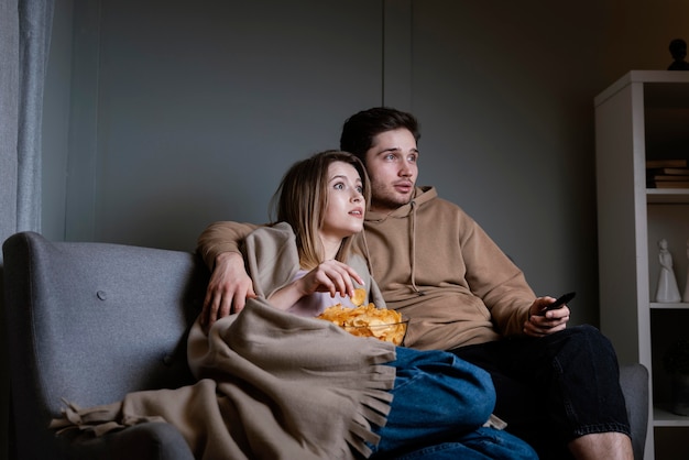 Couple on couch watching tv and eating chips