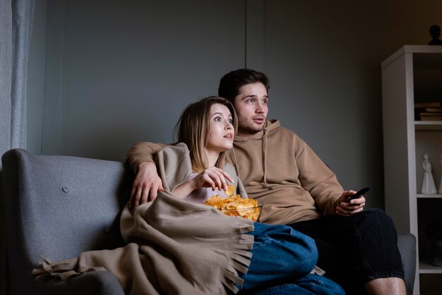 Couple on couch watching tv and eating chips