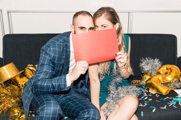 Couple covering faces with paper on couch