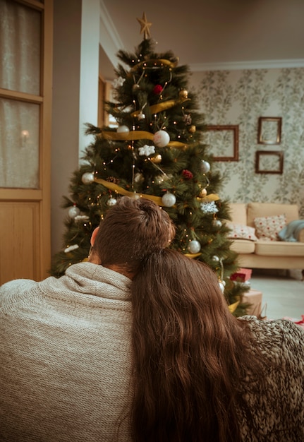 Couple cuddling and looking at Christmas tree