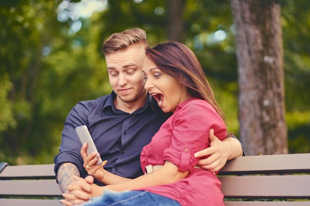 Пара на свидании в городском парке с помощью смартфона и обмена мгновенными сообщениями.