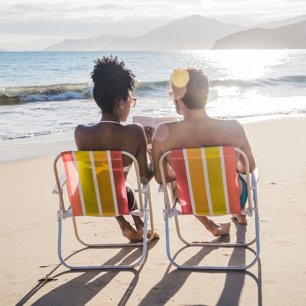 Foto gratuita coppia sulla sedia a sdraio con libro in spiaggia