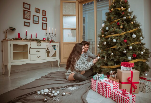 床に座っているクリスマスツリーを飾るカップル