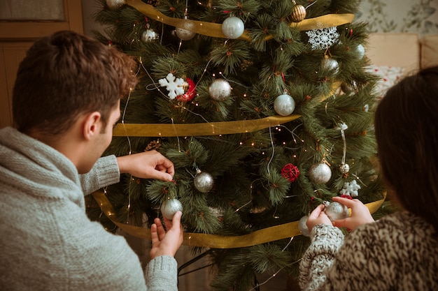 Couple decorating Christmas tree with silver balls