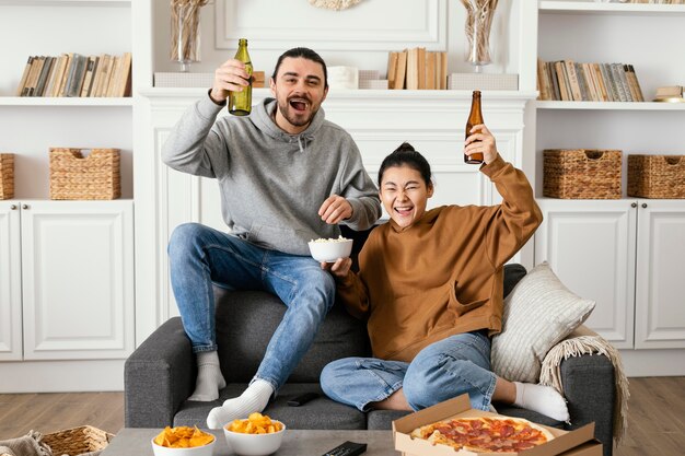 Couple drinking beer and eating snacks indoors