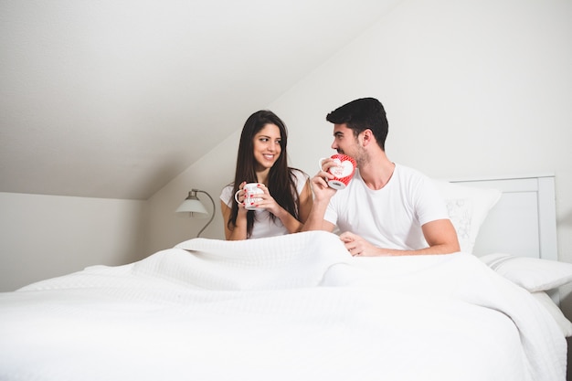 Couple drinking a few cups of coffee on the bed