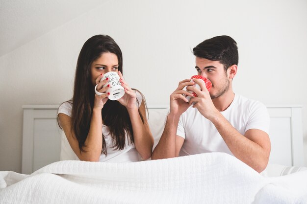 カップルベッドの上にコーヒーを数杯を飲んで