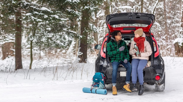 Couple drinking tea while sitting on car trunk