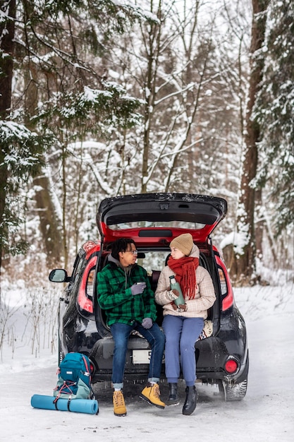 Couple drinking tea while sitting on car trunk