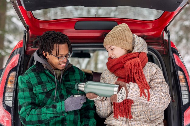 Couple drinking tea while sitting on car trunk