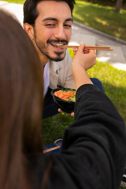 Couple eating bowl of salmon on the grass outdoors