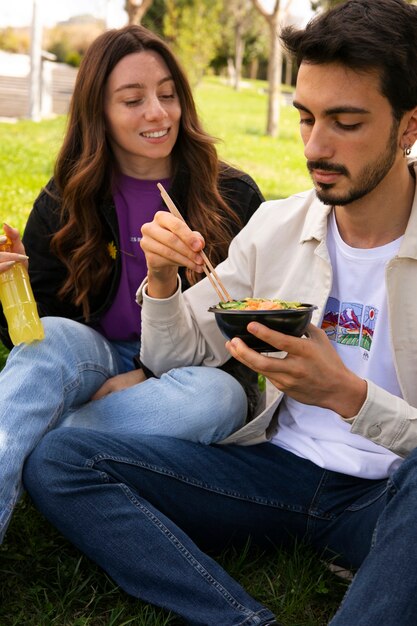 屋外の芝生の上でサーモンのボウルを食べるカップル