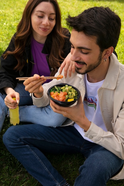Couple eating bowl of salmon on the grass outdoors
