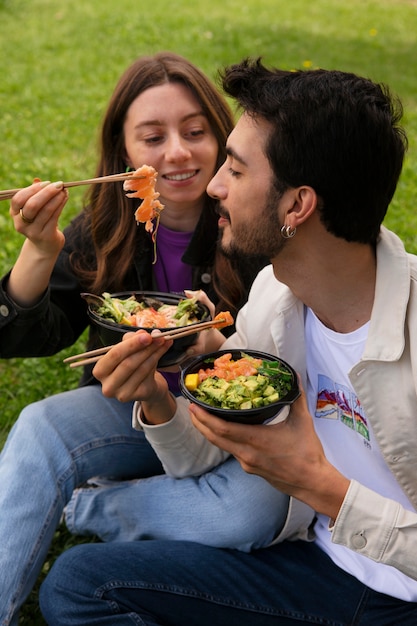 Couple eating bowl of salmon on the grass outdoors