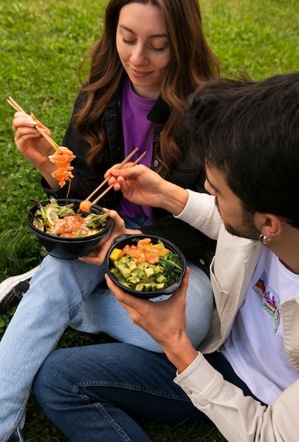 Free photo couple eating bowl of salmon on the grass outdoors