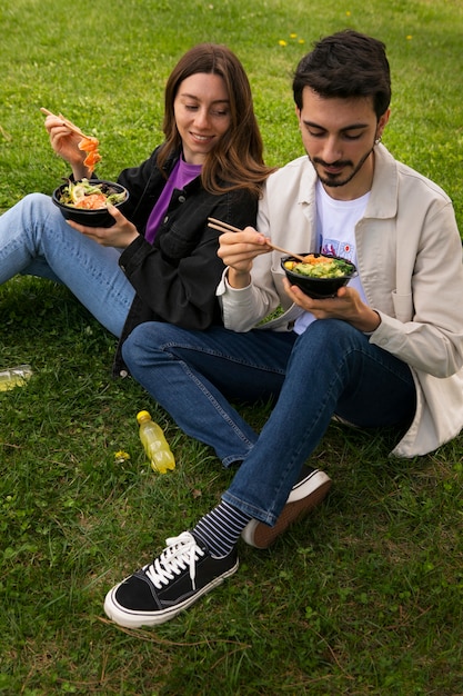 Free photo couple eating bowl of salmon on the grass outdoors