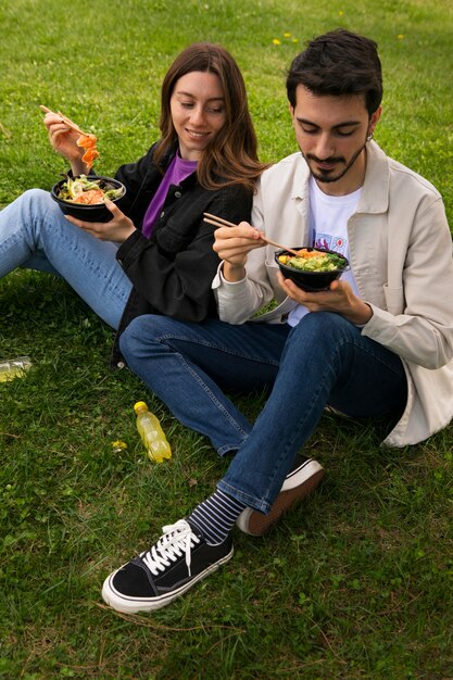 Couple eating bowl of salmon on the grass outdoors