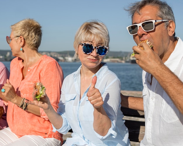 Foto gratuita coppie che mangiano hamburger all'aperto e che danno i pollici in su