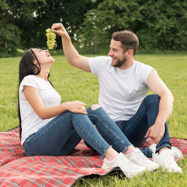 Foto gratuita le coppie che mangiano l'uva con una coperta di picnic