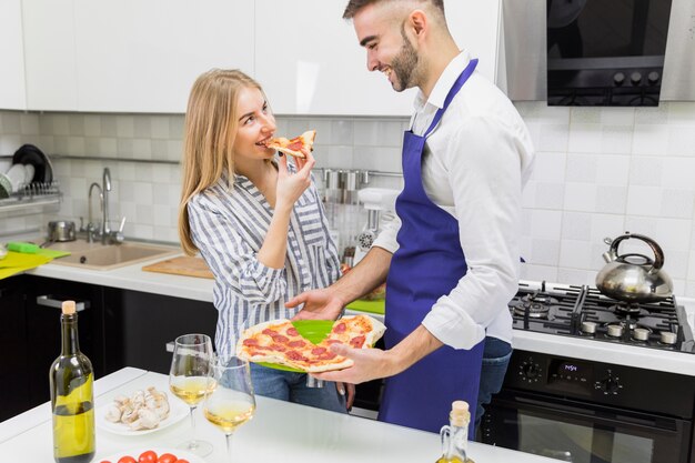 台所でピザを食べるカップル
