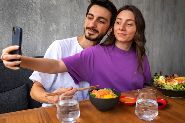 Couple eating salmon dish bowl at the restaurant and taking selfie