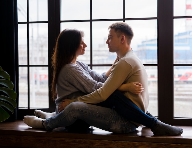 Free photo couple embraced and looking at each other in front of window