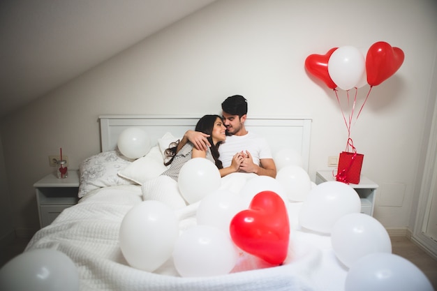 Couple embracing in bed surrounded by balloons