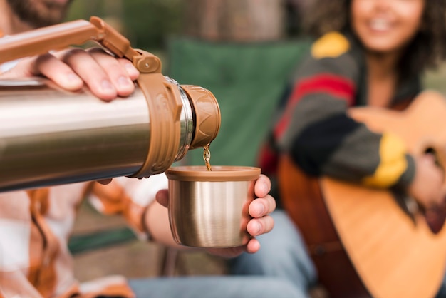 Free photo couple enjoying camping outdoors with guitar and hot drink