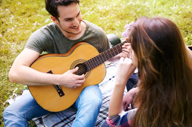 公園でピクニックを楽しんでいるカップル。ギターを弾く男。ロマンチックなデート