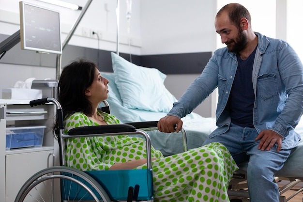 Foto gratuita una coppia in attesa di un bambino nel reparto ospedaliero parla della genitorialità mentre una donna incinta seduta in sedia a rotelle si prepara a partorire. giovani genitori in attesa del parto nella maternità