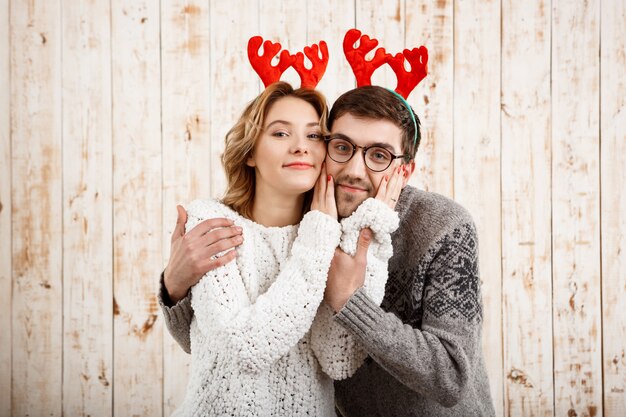 Couple in fake deer horns smiling over wooden wall