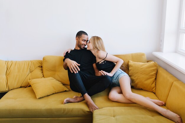 Couple flirting, holding hands, showing love, touching noses, look in the eyes. Loving pair sitting together on the couch. Romance, love relationships, happy faces.