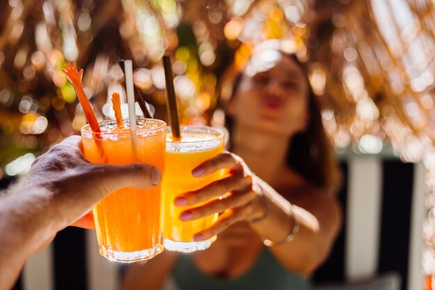 Couple friends clinking glasses of tasty tropical cocktails on sunny day in cafe