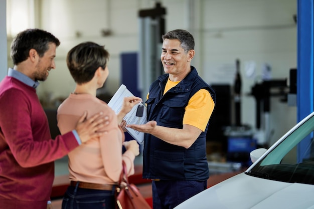 Couple giving car keys to their auto mechanic in auto repair shop Focus is on mechanic