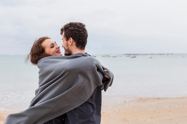 海岸で抱擁するグレーの毛布のカップル
