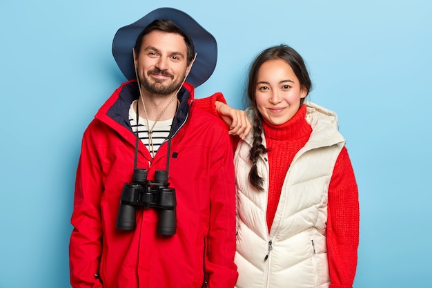 Couple have journey together, stand closely to each other, wear hat and casual clothes, use binoculars for exploring new place