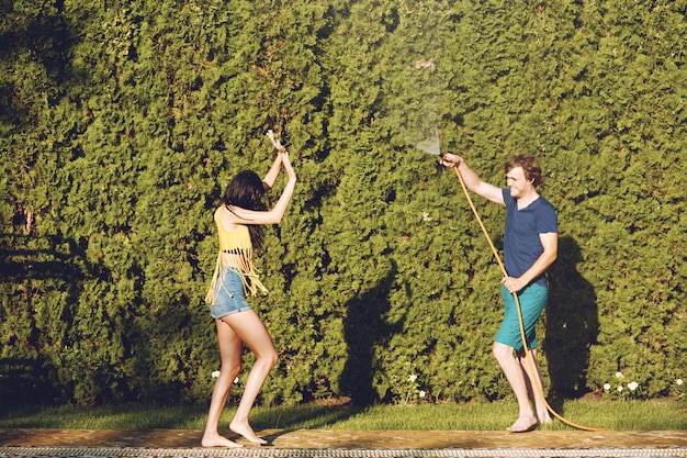 Free photo couple having fun pour each other with garden hose