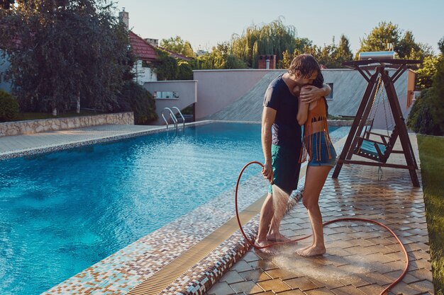 Couple having fun pour each other with garden hose