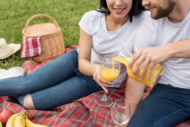 Couple having orange juice on picnic blanket