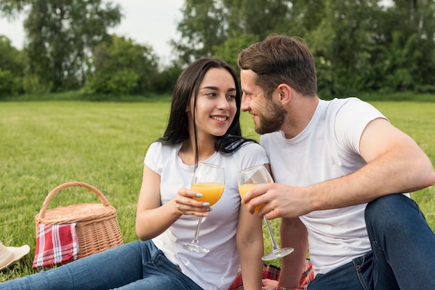Couple having orange juice on picnic blanket