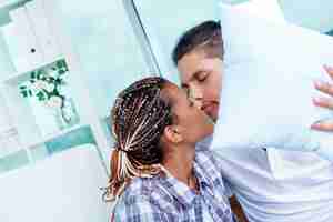 Free photo couple hiding and kissing behind a white cushion