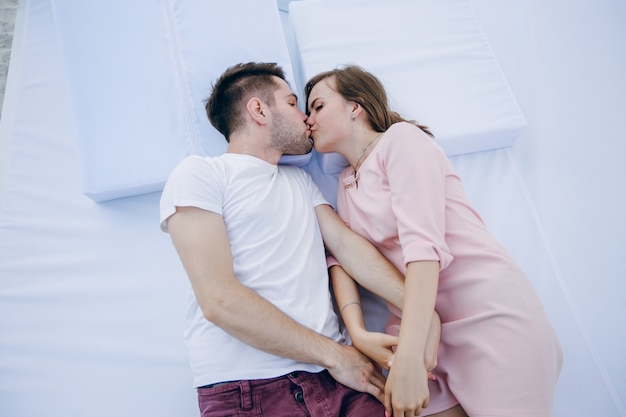 Couple holding hands lying on a double bed kissing