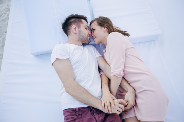 Couple holding hands lying on a double bed with faces close together