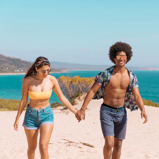 Couple holding hands standing on beach smiling and looking at camera