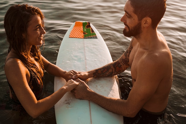 Couple holding hands on surfboard 