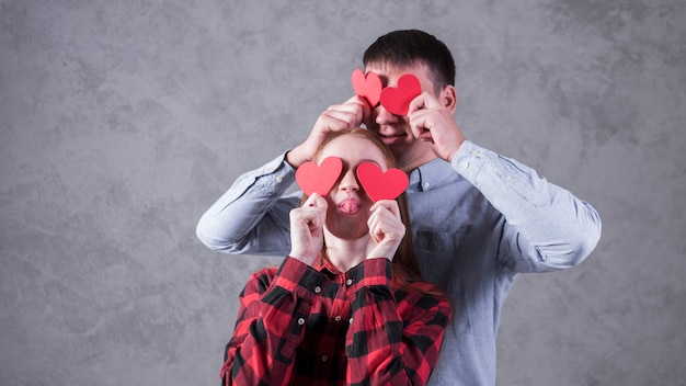 Couple holding paper hearts on eyes 