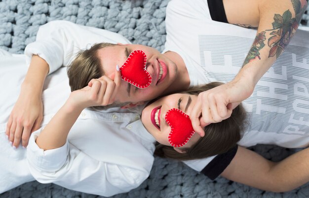 Couple holding red toy hearts at faces 