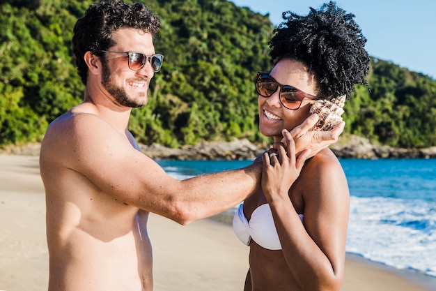 Free photo couple holding seashell at ear